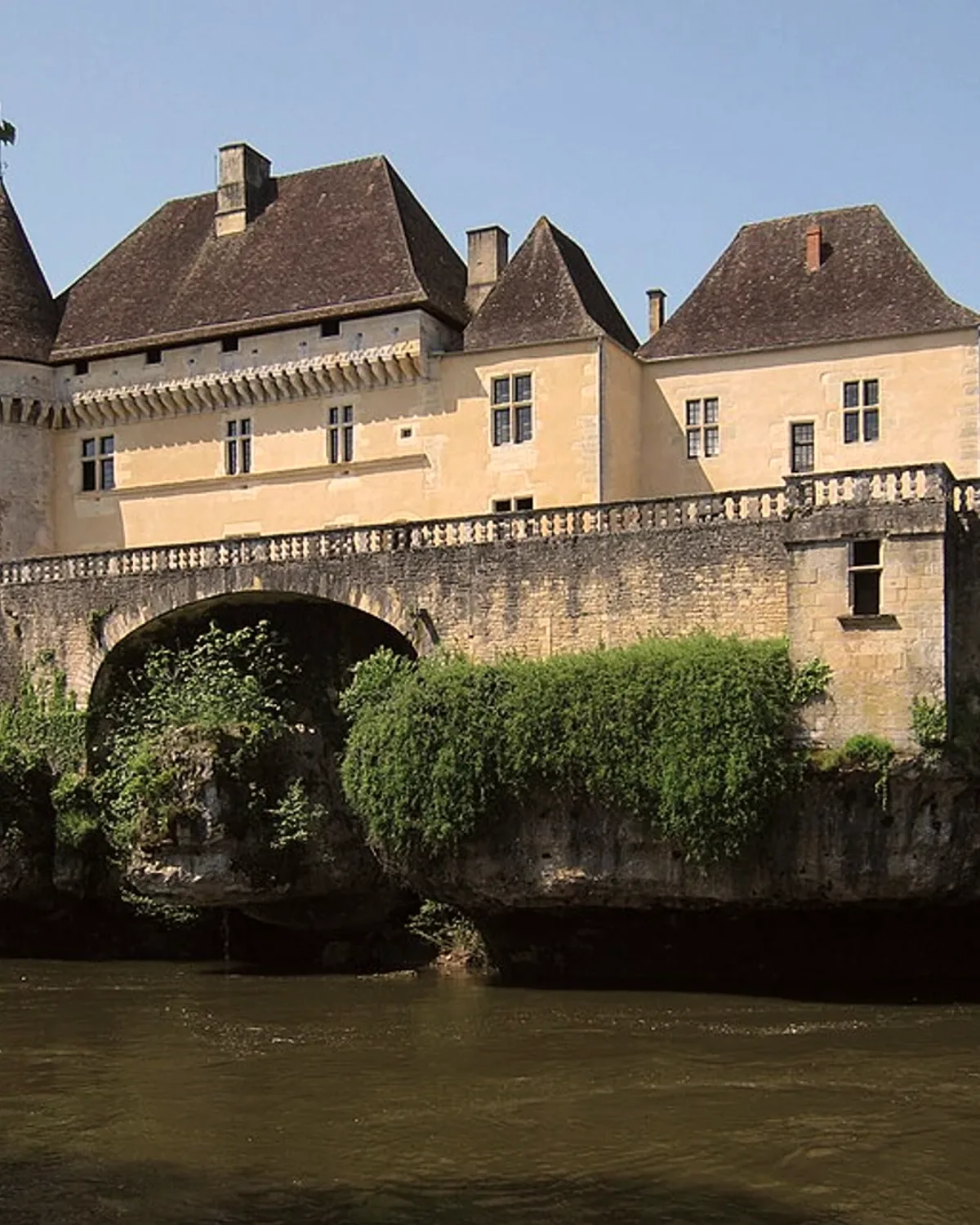 Le château de Losse, ses toits bruns et son pont de pierre au-dessus de la Vézère.
