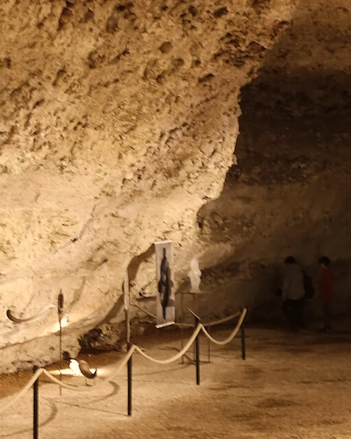 Une galerie de la grotte de Rouffignac, voûte de calcaire éclairée et visiteurs au fond.
